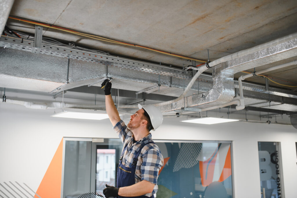 Hvac technician working on air conditioning and ventilation pipes installation in a new office